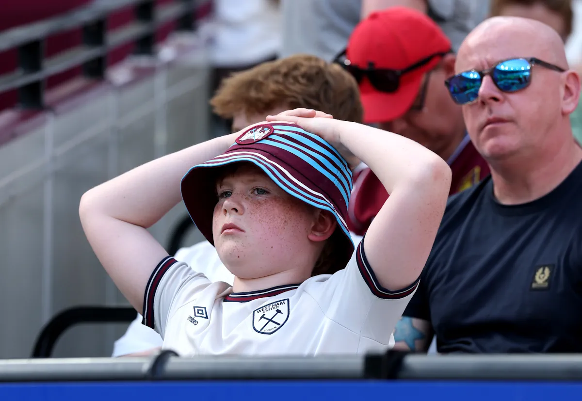 A young West Ham fan holds his head as he watches on from the stands